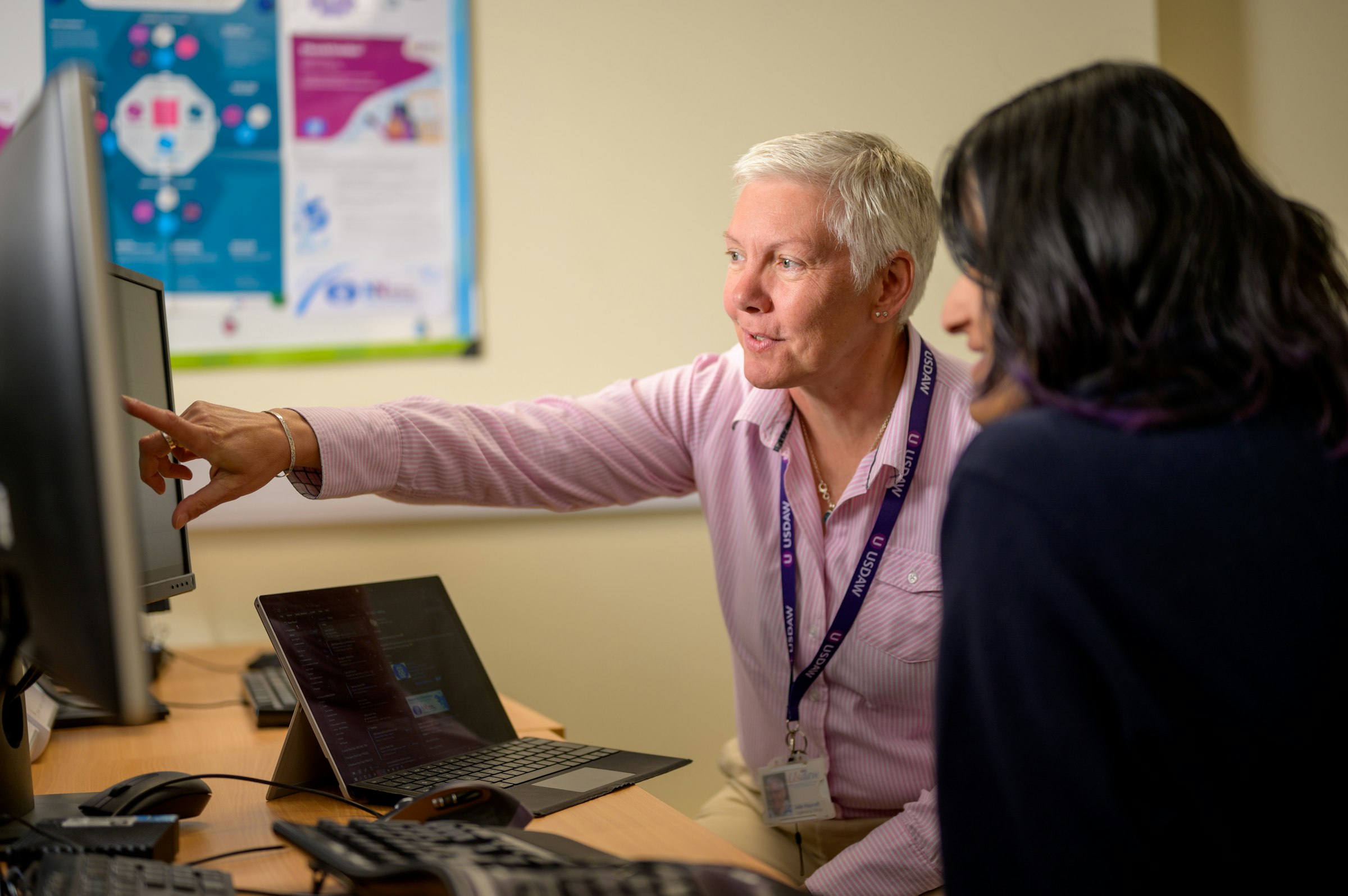 A man pointing at a computer screen while helping a woman