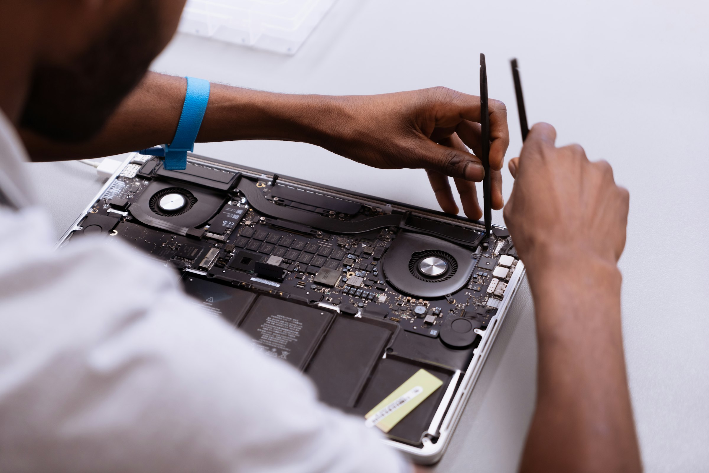 A technician using two pry tools inside an open laptop